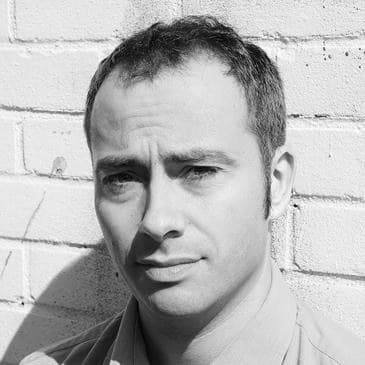 David Adam, looking to camera against a brick wall