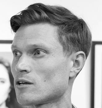 Neil Balmer, looking off to one side in a gallery interior
